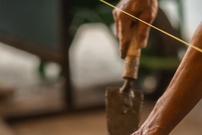 Hands setting a red brick into fresh mortar along a string line.