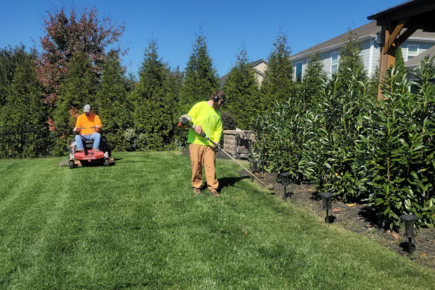 A groundskeeper in a high-visibility shirt edging a planting bed with a string trimmer.