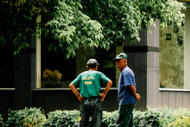 Two crew members in high-visibility shirts standing under trees, talking through the next job.
